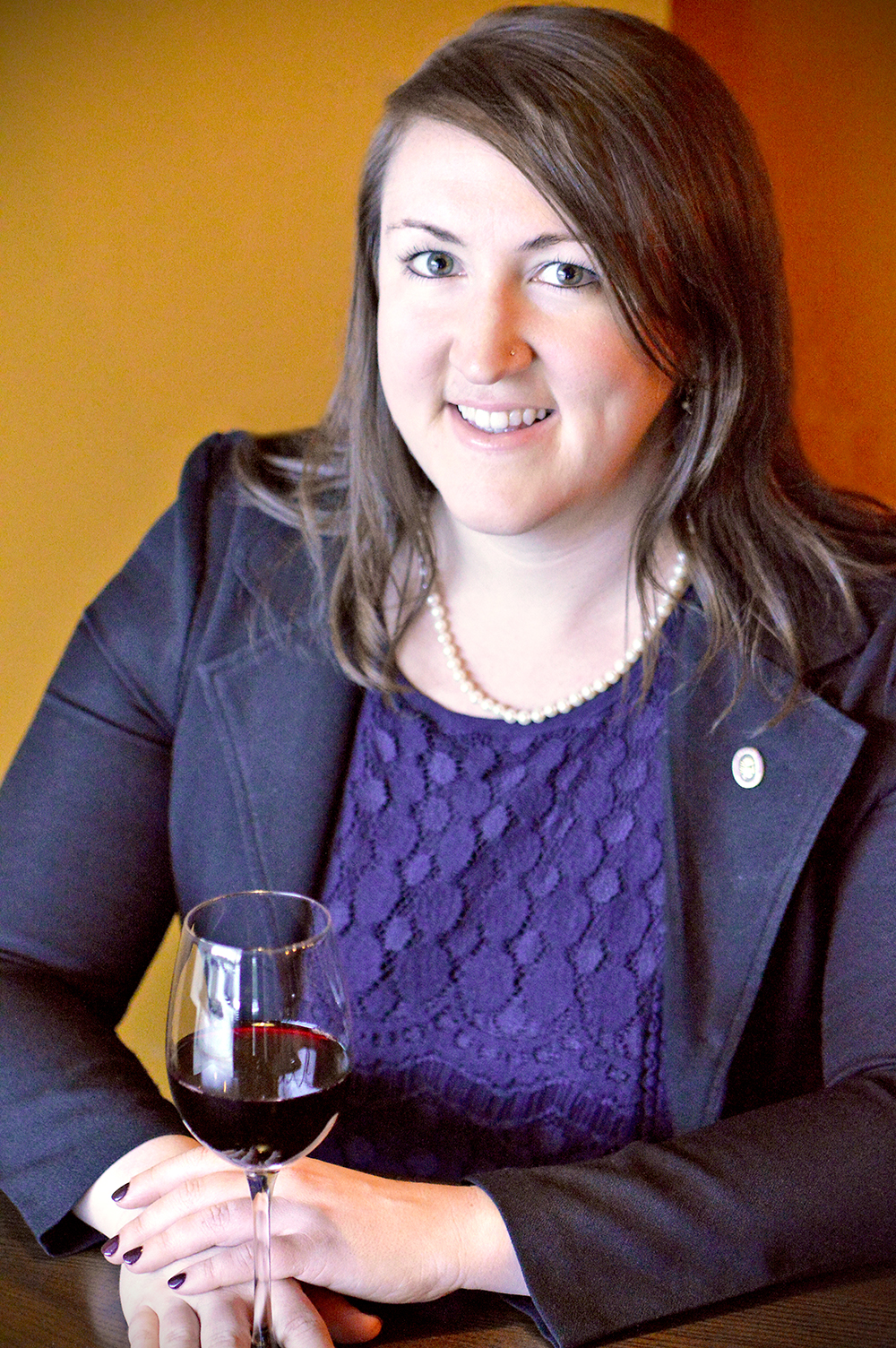 Headshot of a woman with long hair wearing a blue blazer, holding a glass of wine