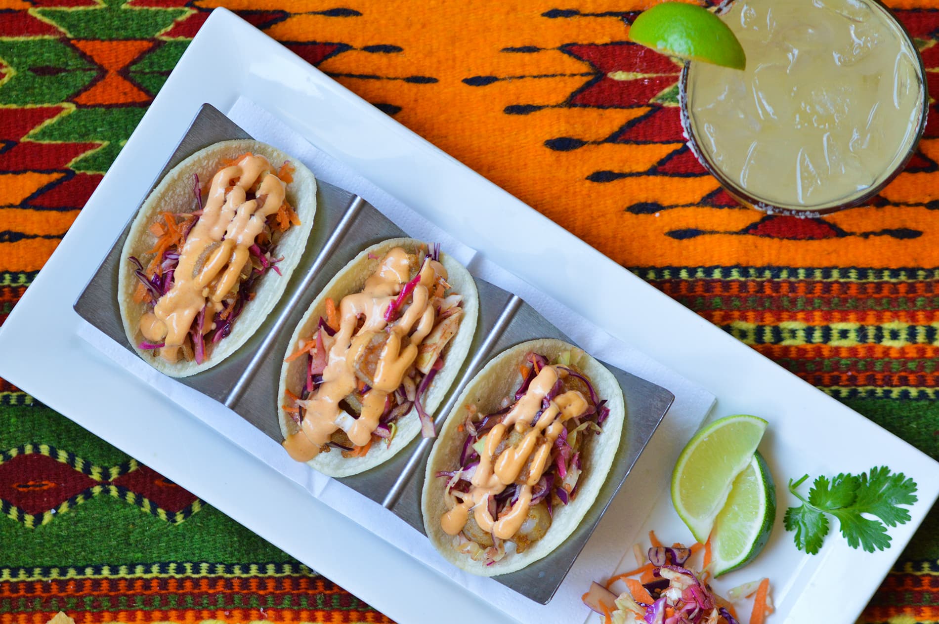 Shrimp tacos with a margarita on a colorful Mexican blanket.